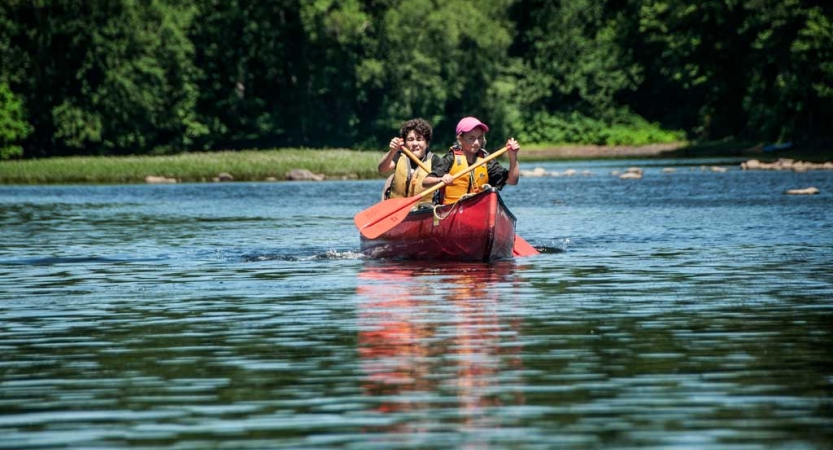 Two people paddle a red canoe on calm water